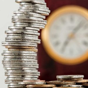 A tall stack of coins against a blurry clock in the background